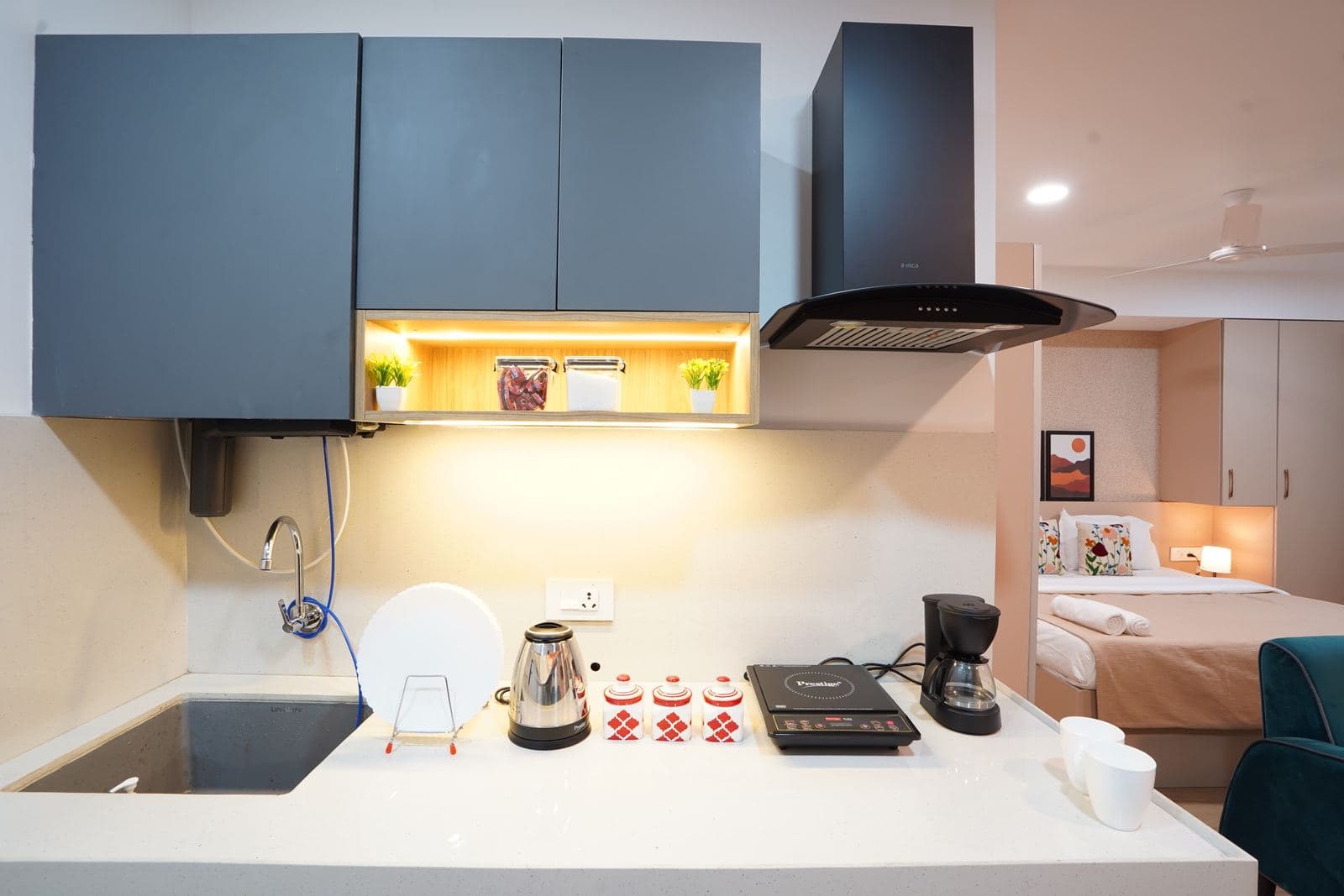 Compact kitchenette with induction cooktop, coffee maker, and an open view into the bedroom
