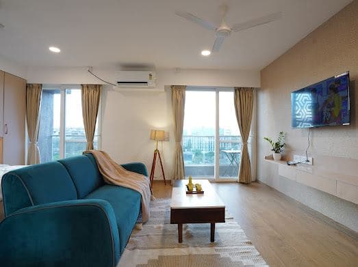 Open living space with a wall-mounted TV, ceiling fan, and large windows overlooking the city