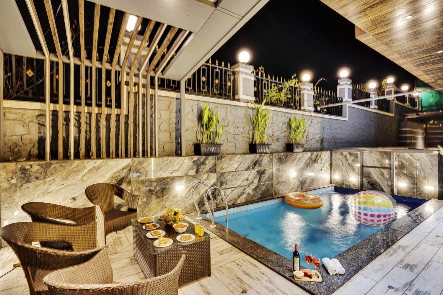 Private night-lit pool with floating pool rings and wicker lounge seating