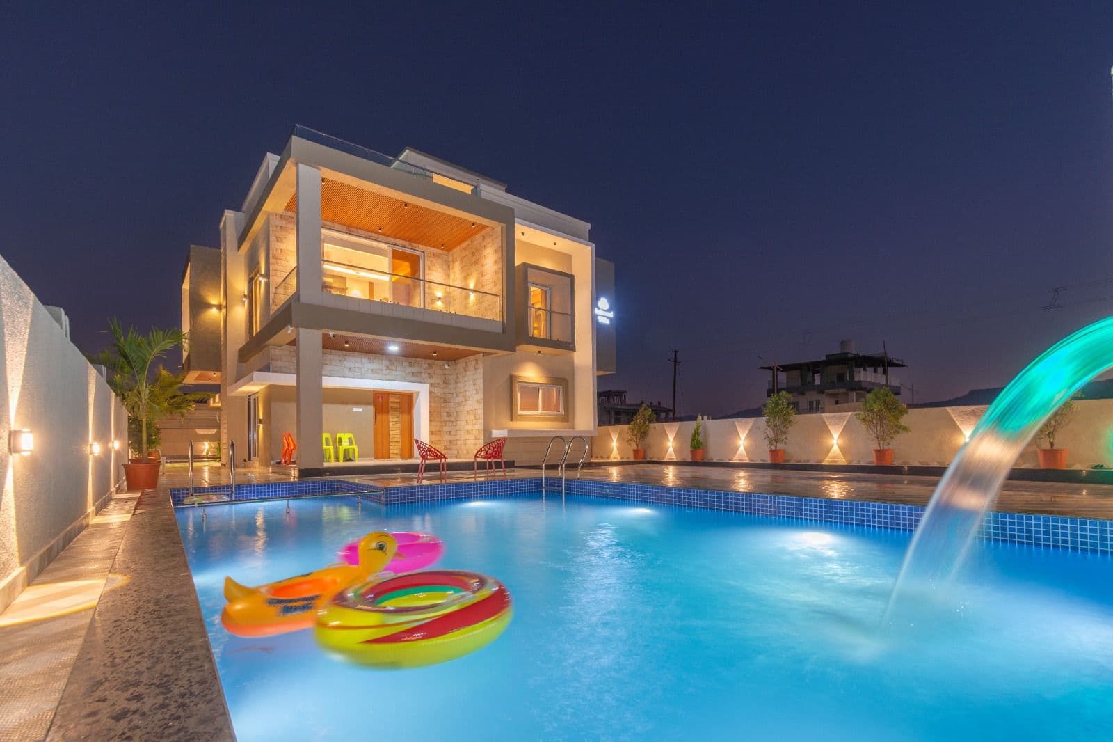 Villa exterior lit up at night with private pool and water-jet feature