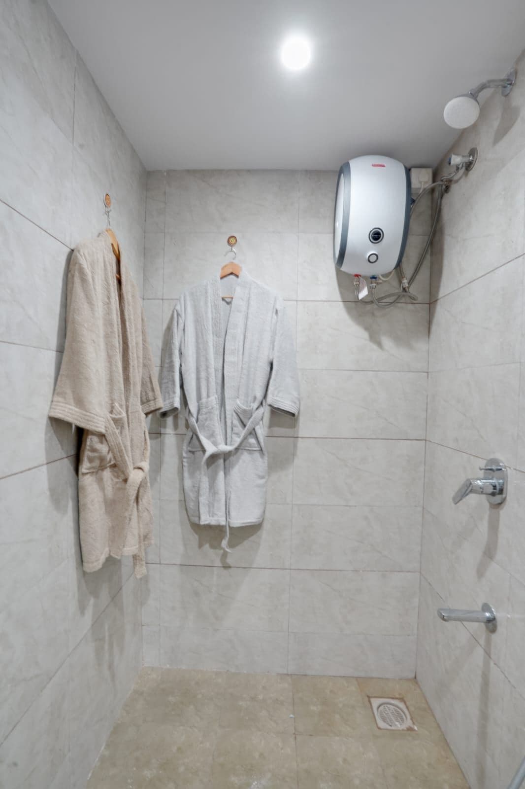 Shower area with bathrobes hanging beside the wall-mounted water heater