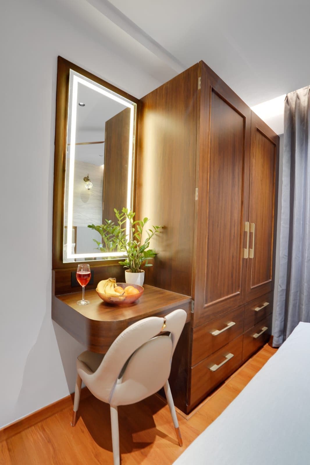 Bedroom dressing nook with a lit mirror, wood wardrobe and fresh flowers